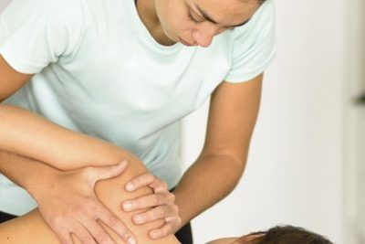 Physiotherapist performing physio treatment on patient's shoulder due to shoulder pain